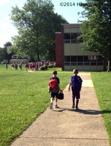 two elementary school kids walking into a suburban school