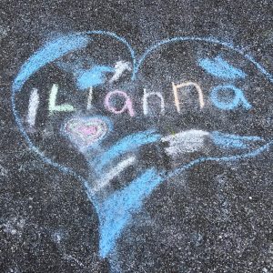A blue chalk heart with a smaller, multicolored heart inside it. "ILianna" is written across the heart in multicolored chalk. Patches of blue and pink fill the heart
